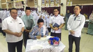 Dr Abdul Rahman menandatangani buku pelawat di SK (A) Datuk Haji Abdul Kadir Hassan, hari ini. Turut kelihatan Hilmy (kiri) serta yang lain.