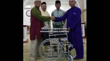 IKHLAS: Hanapi (kiri) menyampaikan sumbangan kerusi roda kepada Mohamad Cek sambil disaksikan ahli lain.