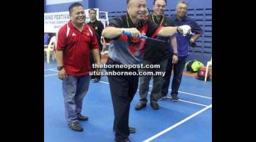 MULA: James melakukan servis sebagai simbolik perasmian Pertandingan Badminton Berpasukan Festival Kuching 2018 sambil disaksikan Hilmy (dua kanan).