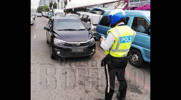 ANGGOTA trafik memberikan saman kepada salah satu kenderaan yang diletakkan secara double parking.