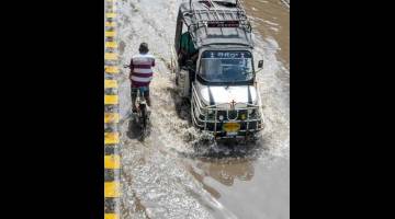 BANJIR: Seorang lelaki mengayuh basikal melintasi sebuah kenderaan ketika mengharungi banjir selepas hujan lebat                       di Amritsar, India kelmarin. — Gambar AFP