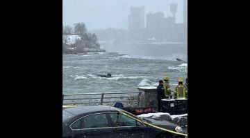 Gambar menunjukkan sebuah kereta hitam dalam air yang mengalir deras di tebing Air Terjun Niagara di sempadan Amerika Syarikat-Kanada kelmarin. — Gambar AFP